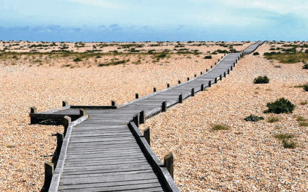 A boardwalk leads into the distance surrounded by shingle.