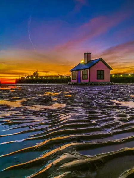 An artwork of a pink house sits in Folkestone Harbour with the tide out at sunset