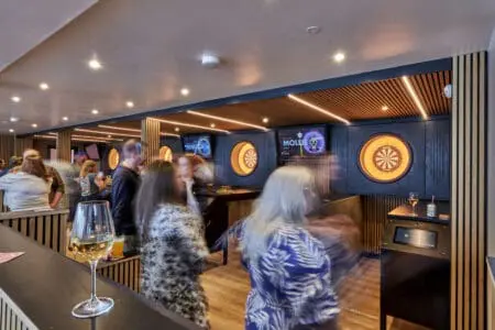 People walk past dartboards and talk to each other