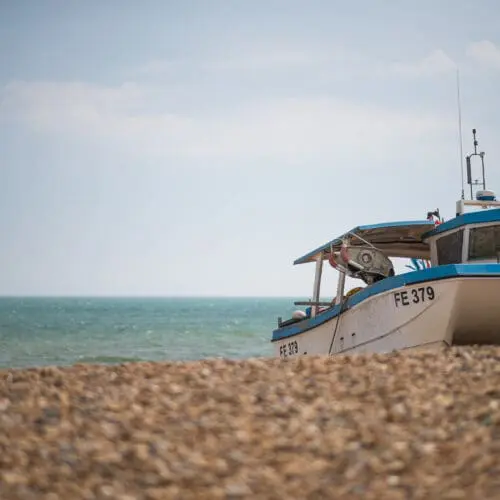 A boat sits on the shingle beach in front of the sea