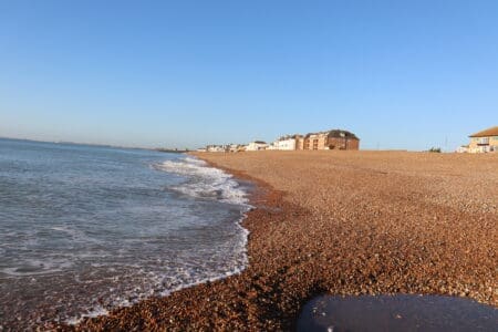 A shingle beach with sea lapping against it and houses in the background