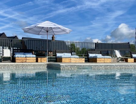 A pool with blue and white striped sunbeds around the side and a blue and white striped umbrella