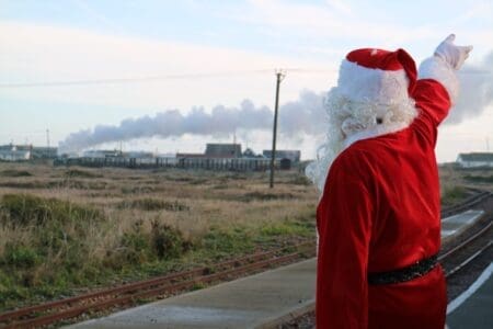 A person in a red and white father christmas outfit waves off a steam train