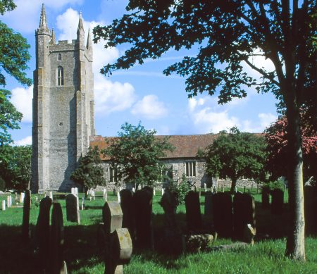 Stone headstones populate a cemetery with trees with a large stone church in the background